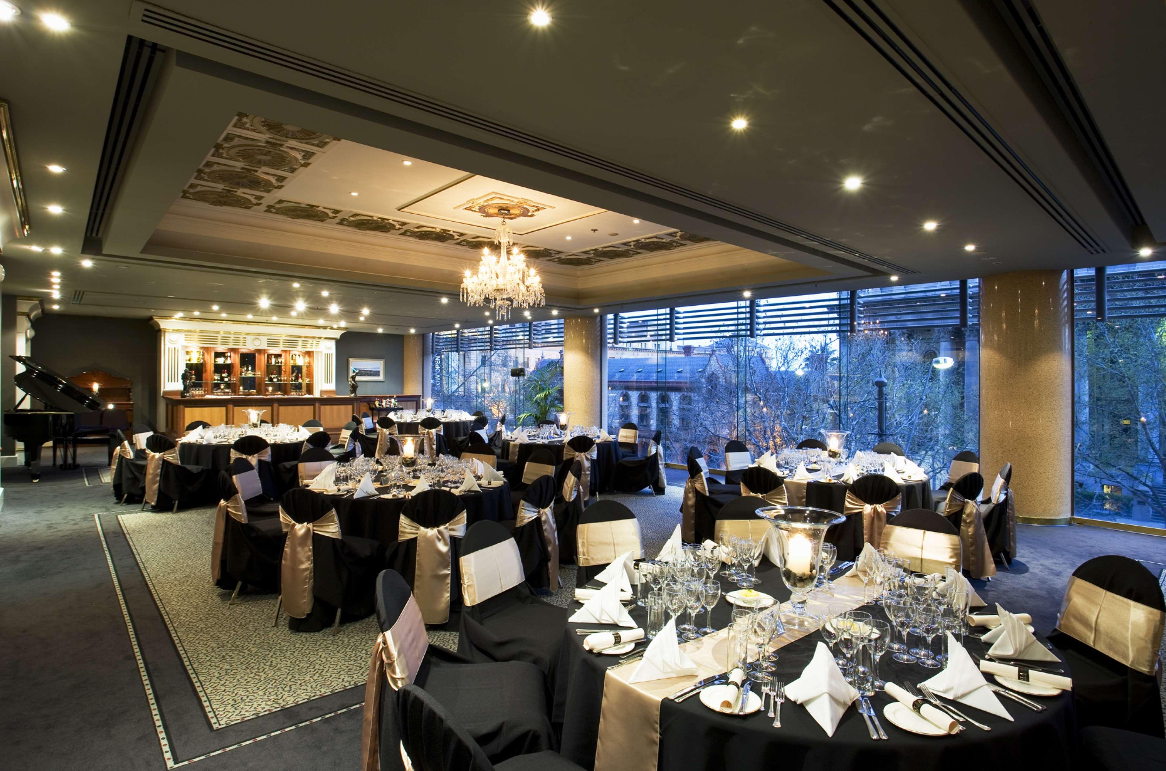 Hotel Stamford Plaza Adelaida Exterior foto The photo shows an elegant banquet hall or restaurant setting. There are several round tables covered with black tablecloths and adorned with gold accents. Each table is set with fine dining utensils, glassware, and neatly folded napkins. In the back