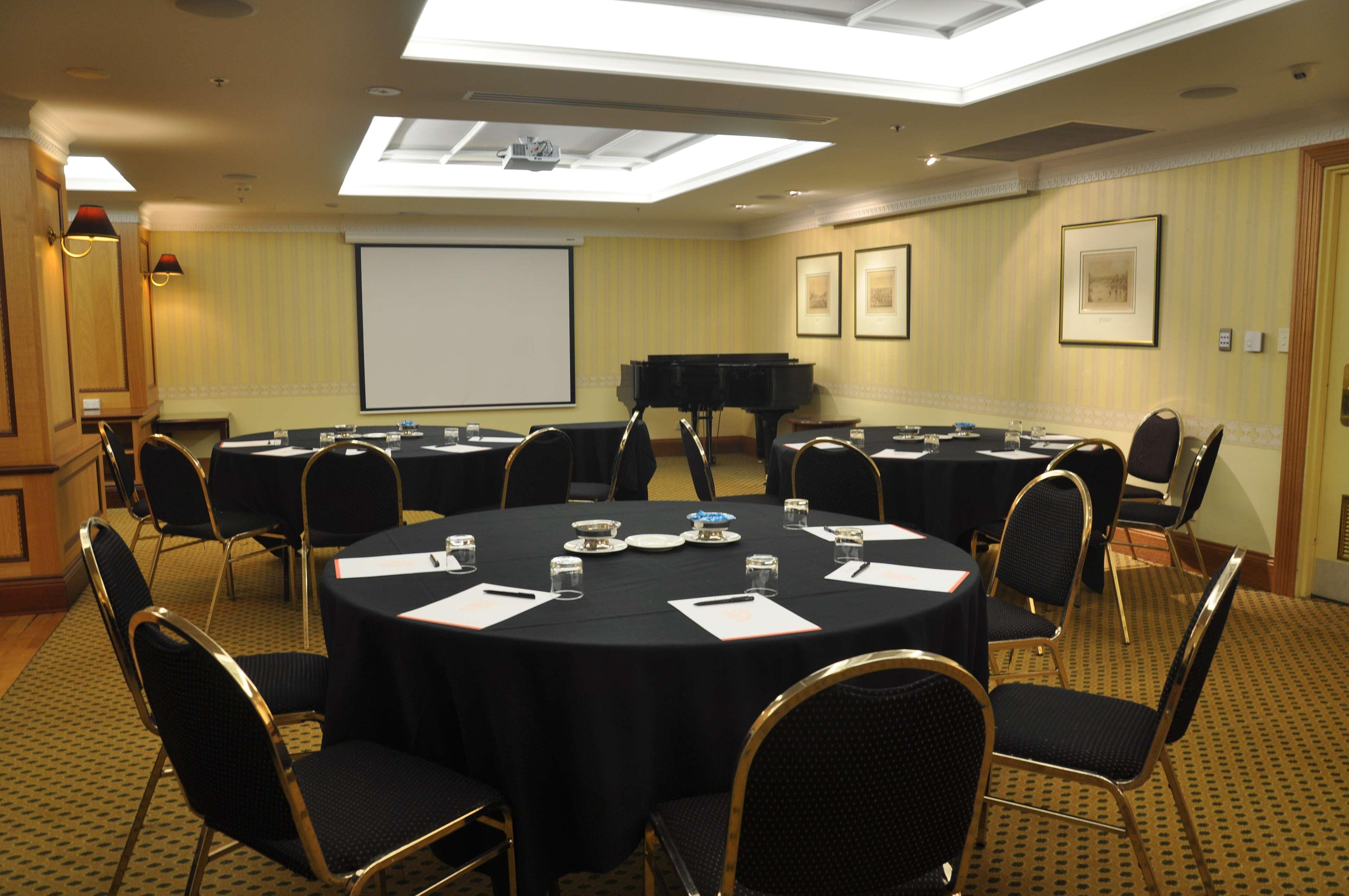 Hotel Stamford Plaza Adelaida Exterior foto The photo shows a conference room set up for a meeting or presentation. There are several round tables covered with black tablecloths, each surrounded by black upholstered chairs. On the tables, there are notepads and glasses of water, indicating tha