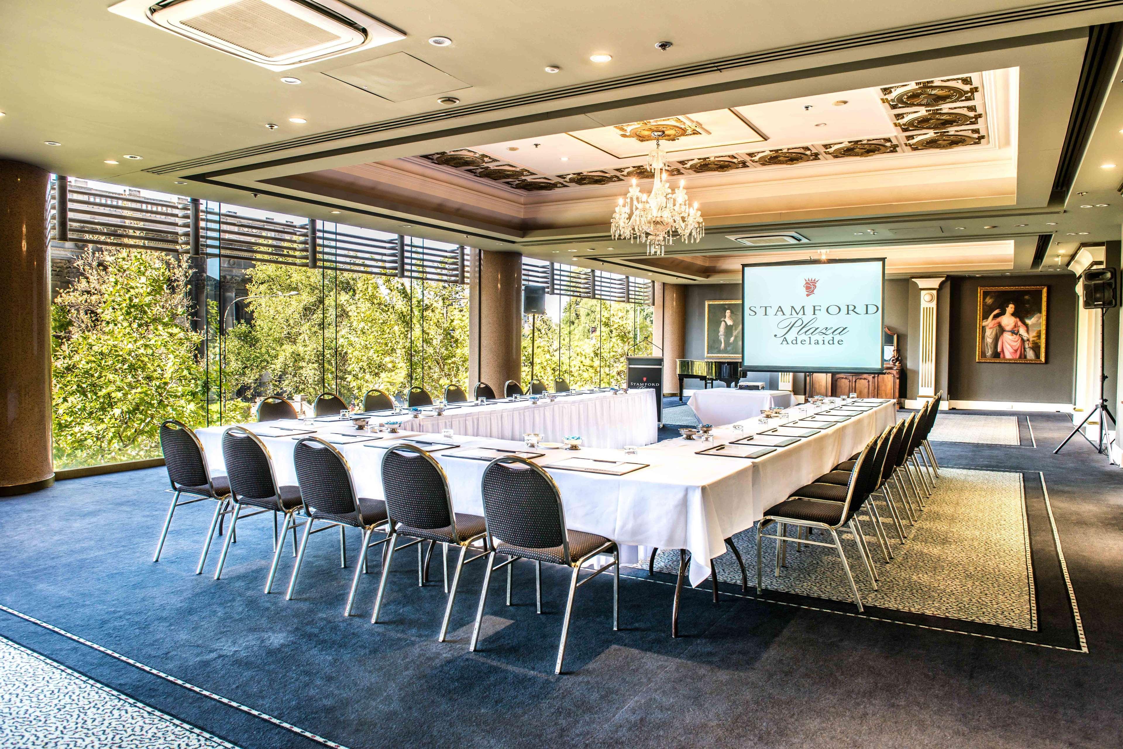Hotel Stamford Plaza Adelaida Exterior foto The photo shows a stylish conference room set up for a meeting or event. There is a long rectangular table covered with a white tablecloth, surrounded by black chairs. A large screen displays the name "Stamford" along with a logo. The room features l