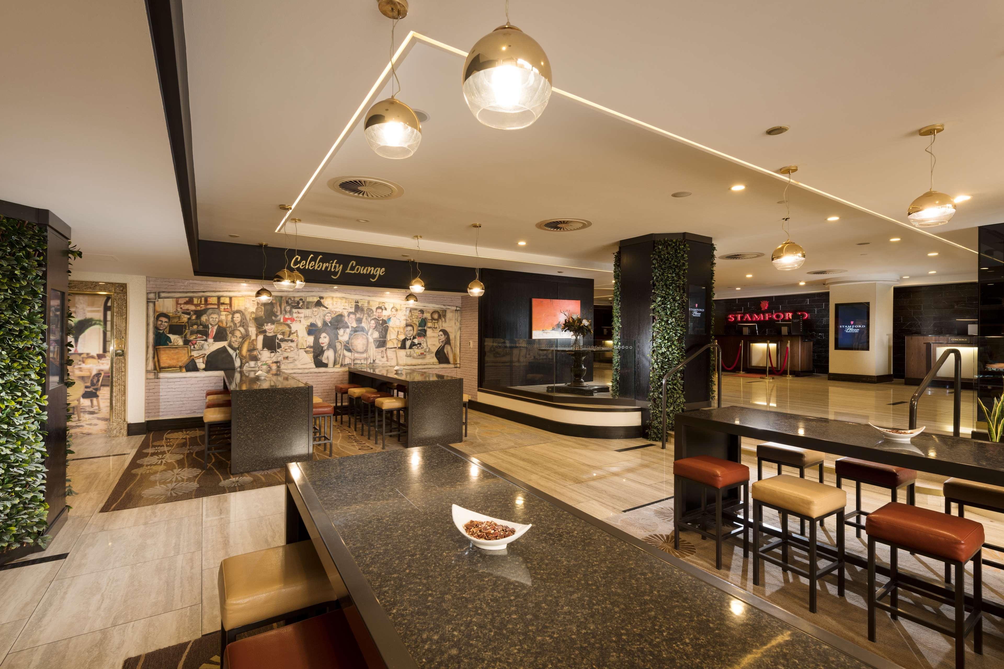 Hotel Stamford Plaza Adelaida Exterior foto The photo shows a modern and stylish interior of a lounge or restaurant area. Prominent features include a long dark countertop with bar stools, and several pendant lights hanging from the ceiling. In the background, there is a mural or artwork that 